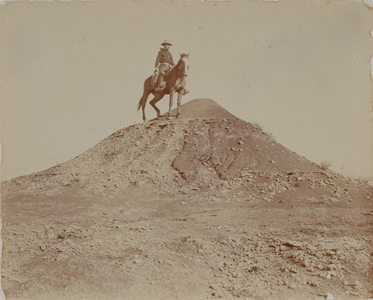 A black-and-white photograph of a man on horseback at the top of a hill.