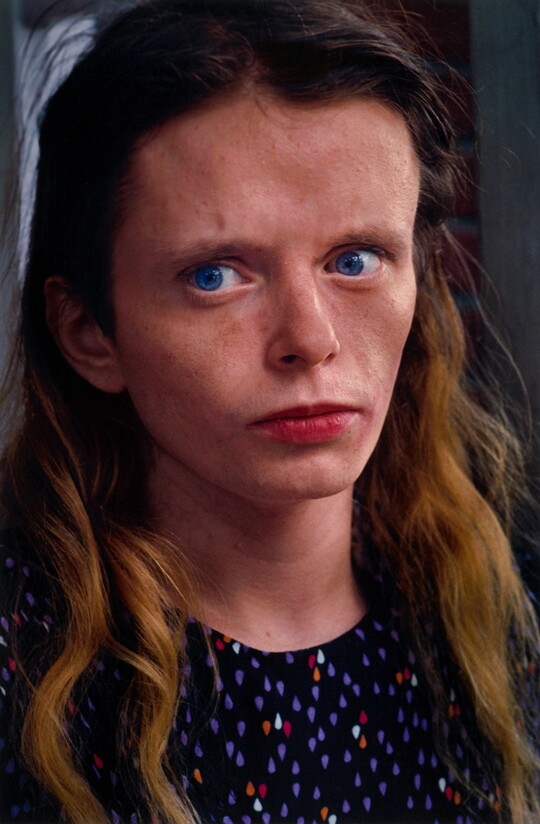 A color portrait photograph of a young White woman with blue eyes looking off to the side, freckles scattered across her face, long hair dark blonde, wearing a polka-dot top.