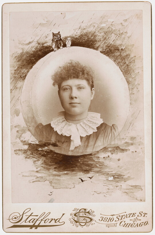 A sepia-toned, circular portrait photograph of a woman with curly hair in a lace, high-collared dress and decorative border that includes owls.