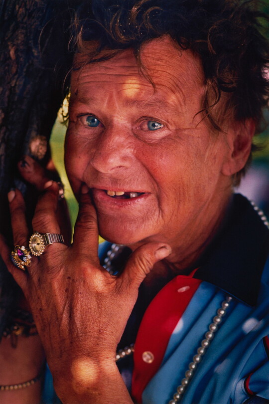 A color portrait photograph of a White adult with curly hair and a surprised expression, touching their face with ring-clad fingers.