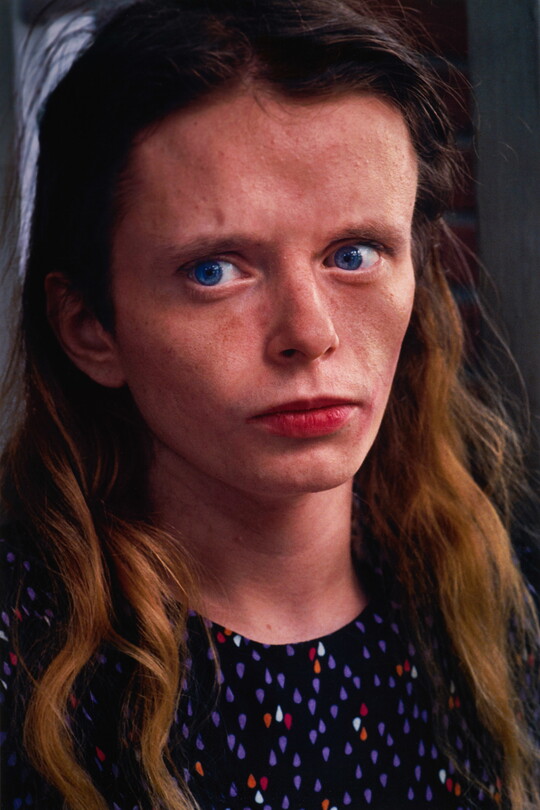 A color portrait photograph of a young White woman with blue eyes looking off to the side, freckles scattered across her face, and long hair wearing a polka-dot top.