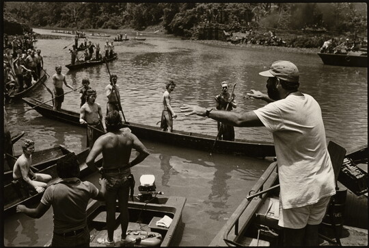 A black-and-white photograph of a man addressing a group of people in boats on a river.