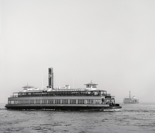 A black-and-white photograph of a large ferryboat on the water under a clear sky.