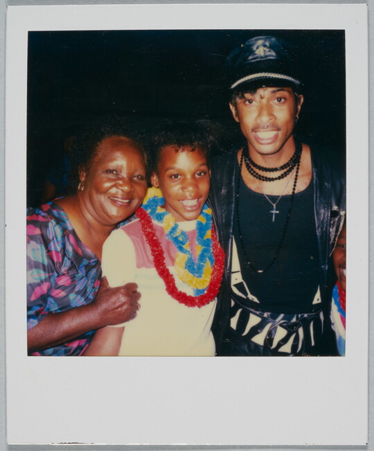 A color Polaroid photograph of a smiling Black woman, girl, and man posed standing together.