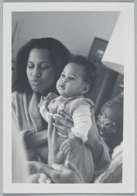 A candid black-and-white photograph of a Black woman holding a baby.