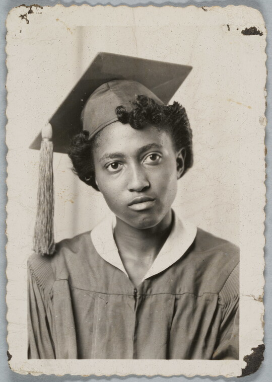 A black-and-white studio photograph of the head and shoulders of a Black woman in a graduation cap and gown.