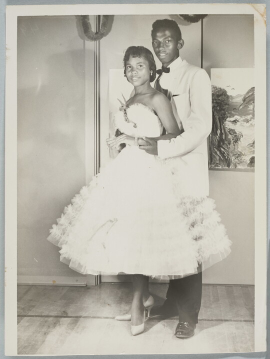 A black-and-white photograph of a Black couple in formal dress at a dance.