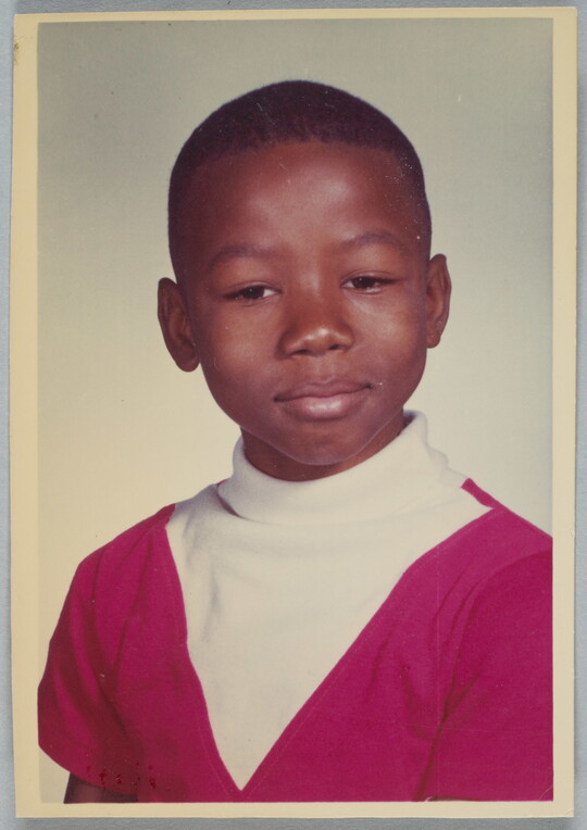 A color school photograph of a Black child with short hair wearing a white and red turtleneck.