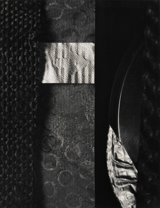 A black-and-white abstract photograph of materials of contrasting textures laid flat to form shapes.