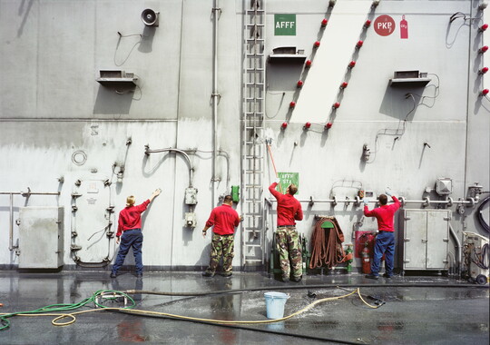 A color photograph of four soldiers washing the side of a large ship.