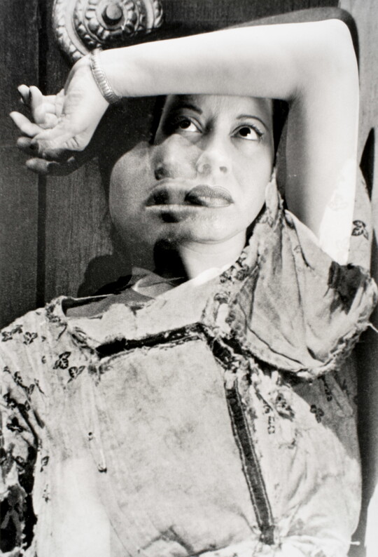 A black-and-white, double-exposure photograph of two portraits of women posed with their arm over their heads and gazing upward.