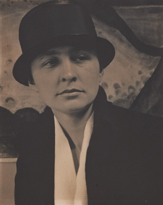 A sepia-toned photograph of a White woman wearing what looks like a top hat, and white blouse under a dark jacket.
