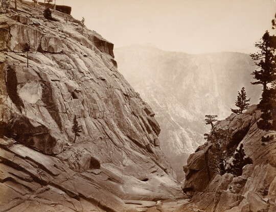 A sepia-toned photograph of a dry creek bed between two steep rocky hills.