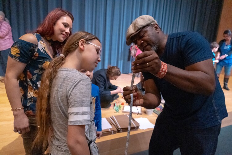 An artist shows a measuring tape to two visitors.