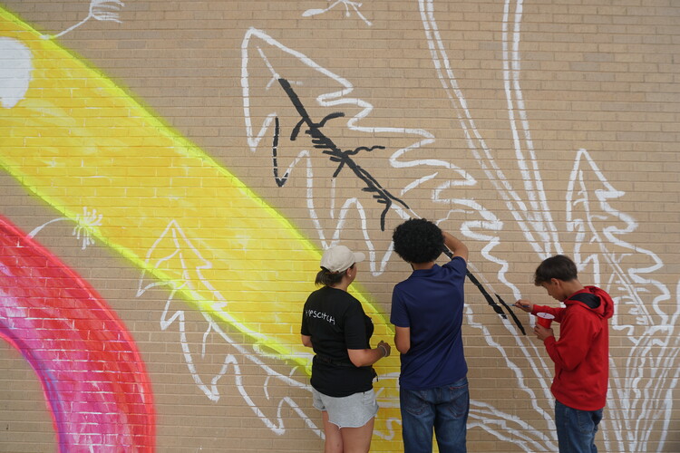 Middle school students paint a mural on to a brick wall.