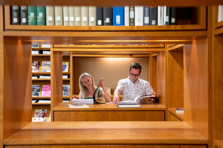 Two adults look at books in the Carter Library as viewed through the stacks.
