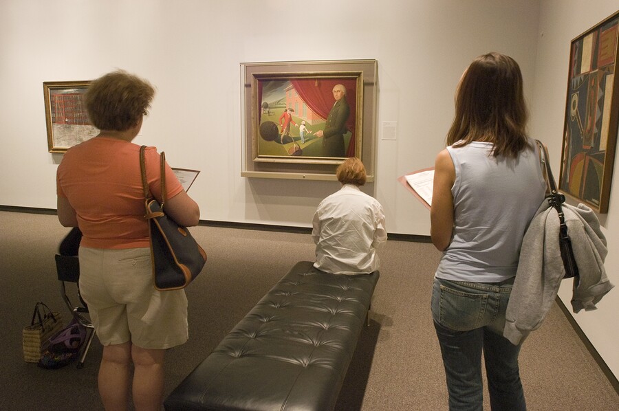 Three adults in a gallery look at a painting.