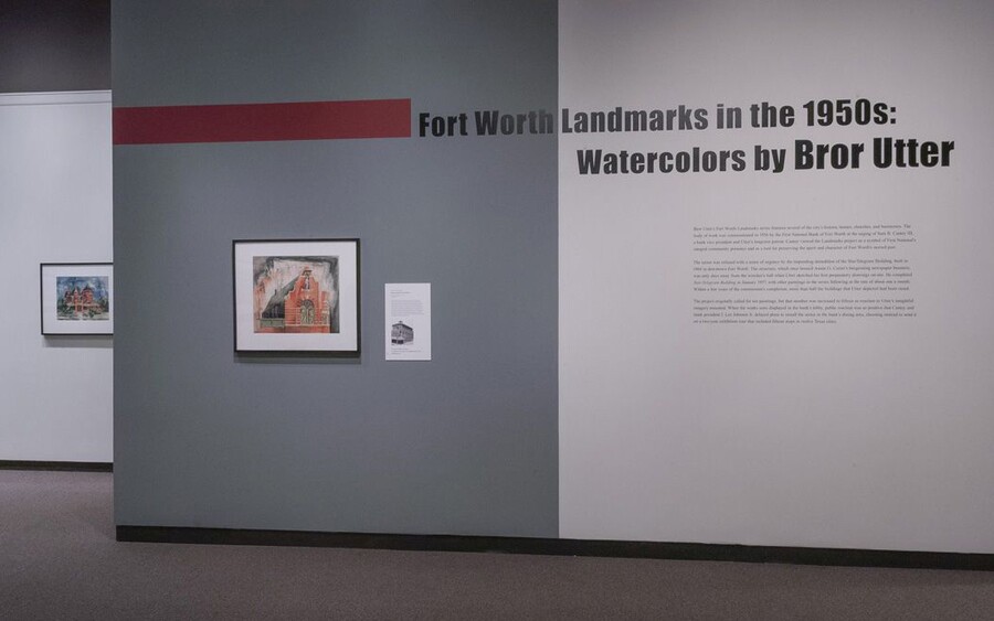 Exhibition title wall; the left half is dark gray and features a framed watercolor of a church; the right half is light gray and features exhibition text.