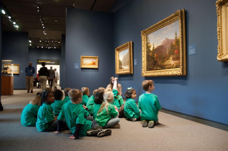 School children sit on the floor of a Carter gallery in front of several paintings.