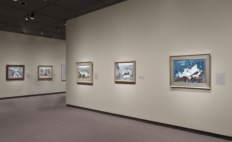 Cream-colored gallery walls with framed paintings hanging on the two visible walls.