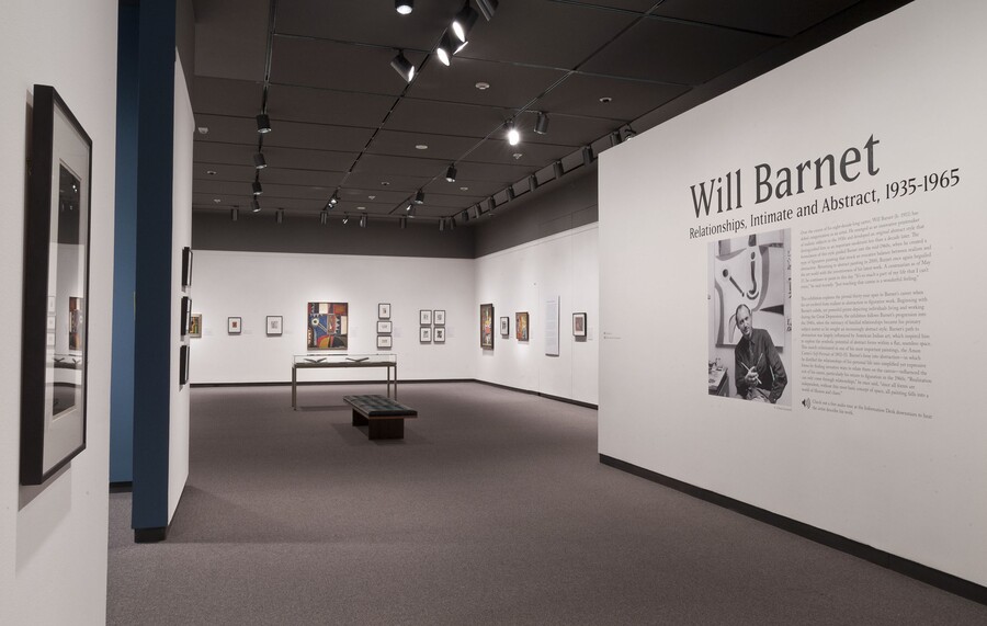 View of gallery; wall on the right has the title graphic and a photo of the artist; the other two visible walls feature framed artwork.
