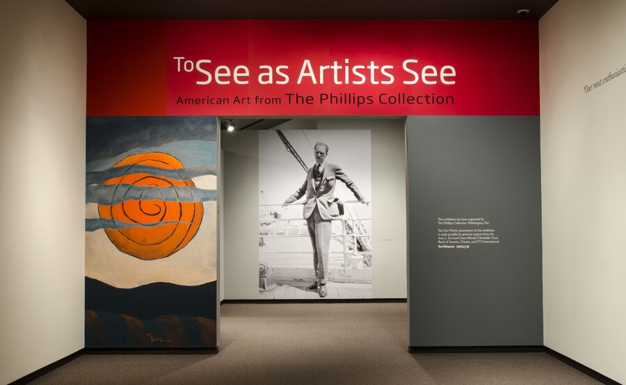 Title wall and entrance to an exhibition; to the left of the entrance is a graphic illustration of a sun behind a cloud; through the entrance is a large black-and-white photo reproduction of a man in a suit leaning against a railing.