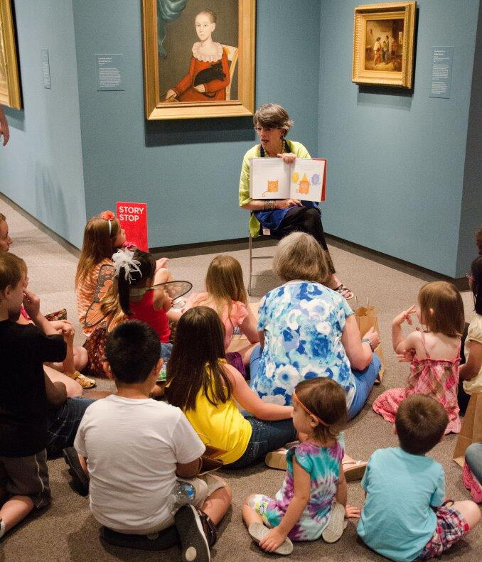 A Carter educator sits in front of an artwork and reads a story to a group of children sitting on the floor.