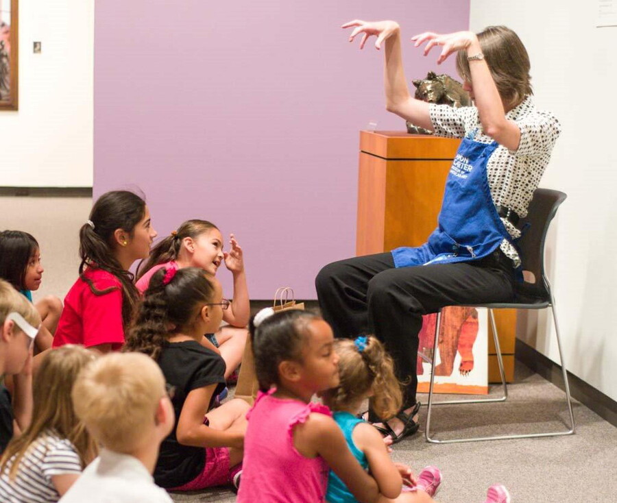 A Carter staff member sits in a chair in front  of group of children seated on the floor.