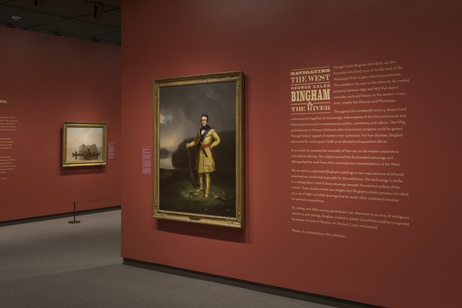 A dark orange-red wall featuring introductory text to the right of a gold-framed painting of a man standing on a hillside.