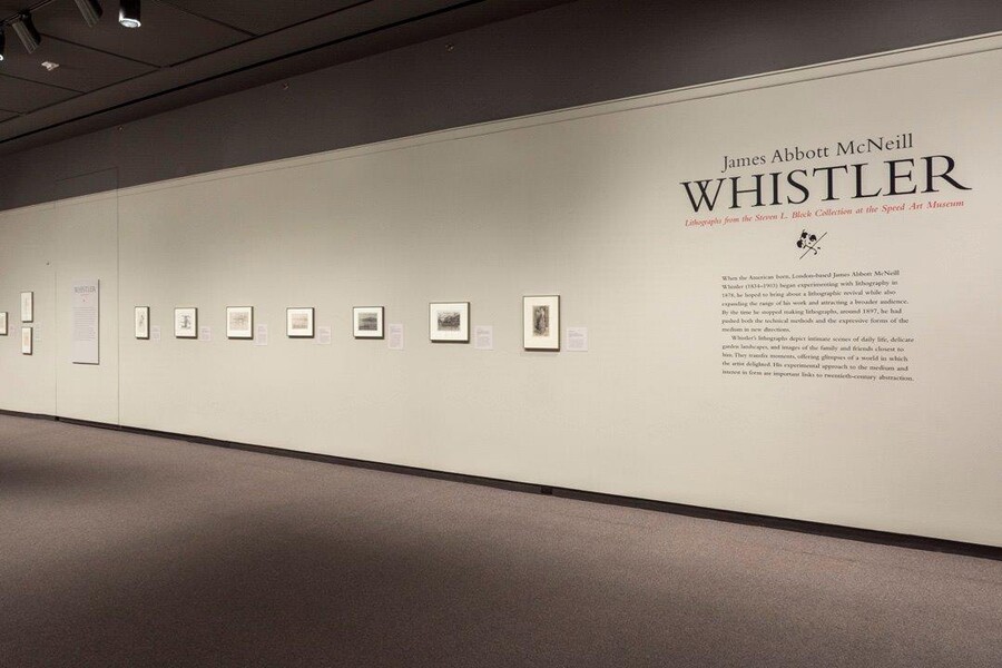 View of gallery showing exhibition title and introductory text and a row of framed prints to the left hanging on a white wall.