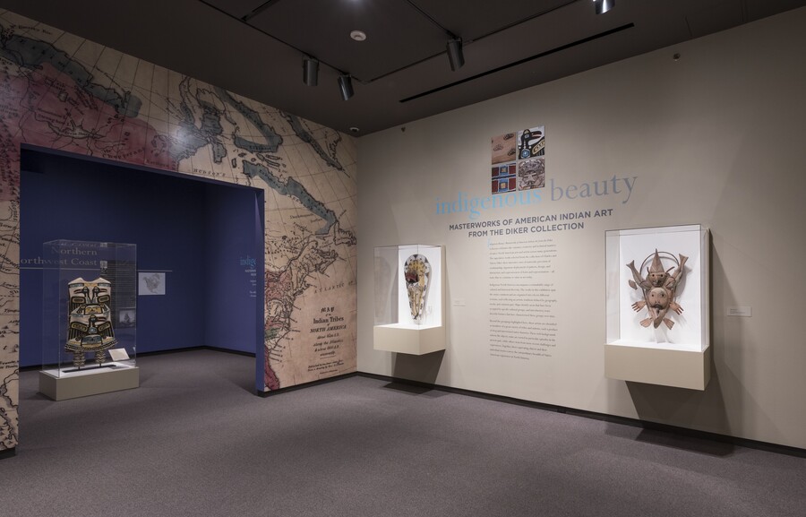 Exhibition entrance; on the right is the title wall and introductory text with two display cases containing native American objects; the entrance wall features a map of North America; through the entrance is a display case containing an object.
