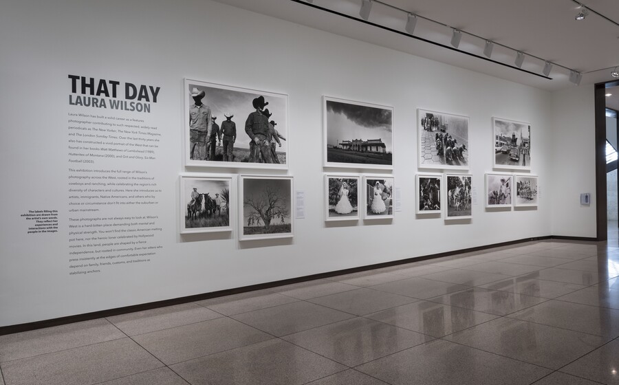 White gallery wall with exhibition title and text to the left; 12 framed photographs are arranged in four groups of three.