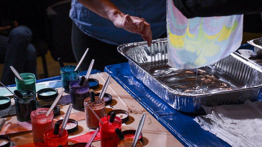 Jars of paints sit on a worktable as hands pull a piece of handmade paper out of a basin of water.
