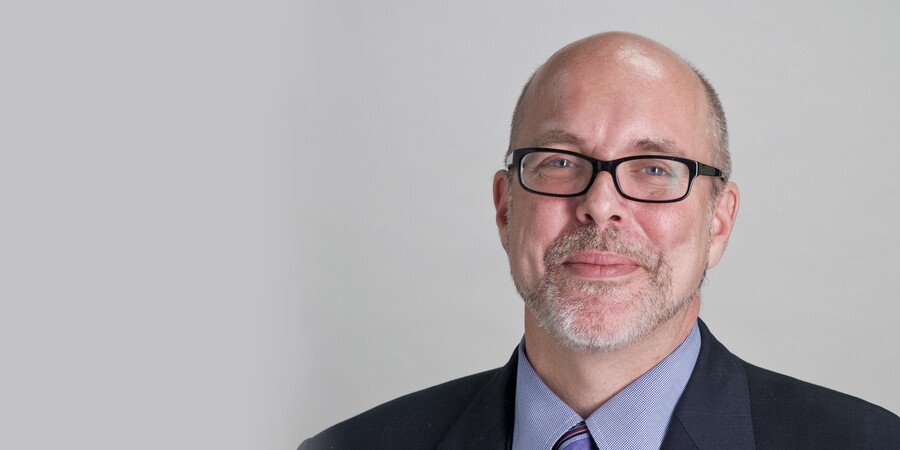 Headshot of a White man, bald with a goatee and black-framed glasses.