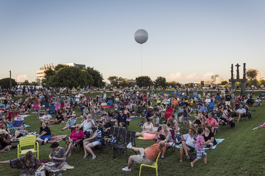 A large crowd of people sit and mingle on the grassy lawn in front of the Carter.