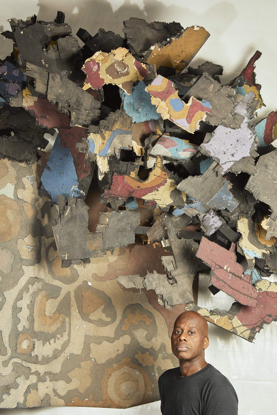 A Black man stands under an abstract installation high on a wall.