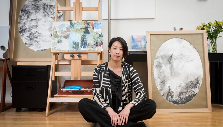 Artist Lingchia Tsai sits on the floor of her studio in front of art and easels.