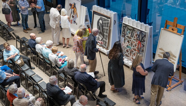 A crowd of people on folding chairs in the Carter's main gallery in front of easels displaying artwork.