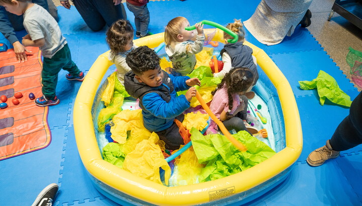 Five small children sit in a baby pool filled with tissue paper and toys in the Carter's Atrium.