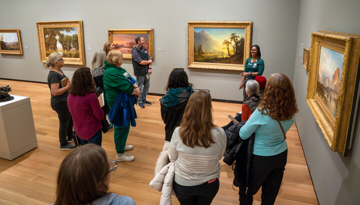 A group of adults stand in a Carter gallery listening to a Museum educator.