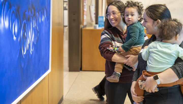Smiling adults holding babies on their hips look at artwork in a Carter gallery.