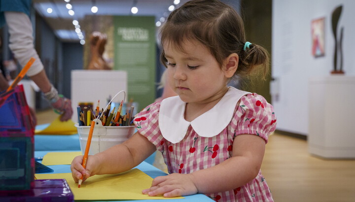 A child draws on a sheet of paper at a table in a Carter gallery.