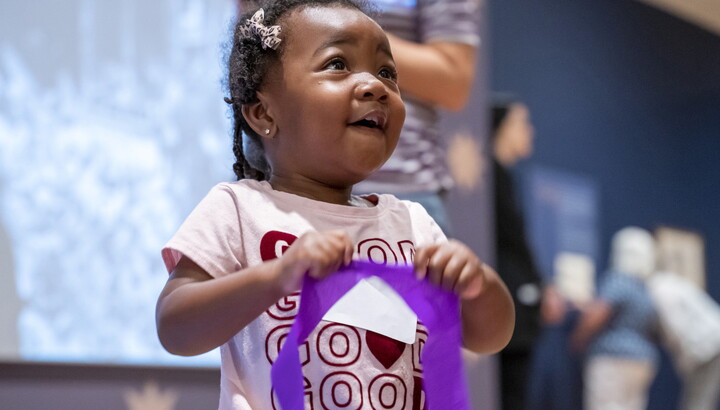 A black child smiles as she holds a purple streamer in a Carter gallery.