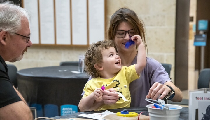A White child sits on the lap of a woman as they laugh and make art at a table in the Carter's Atrium.