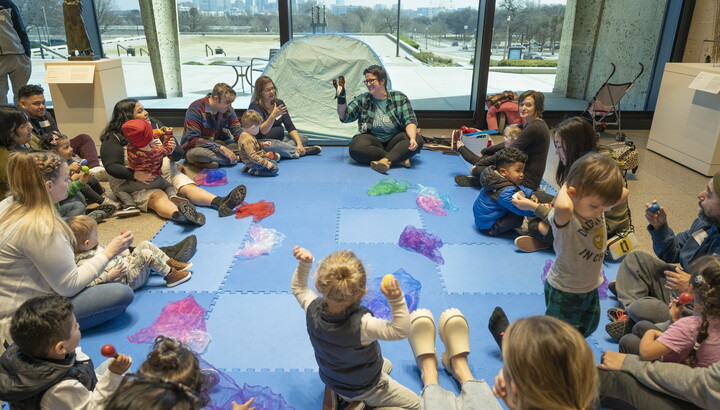 A group of adults and children are seated on the floor of a Carter gallery around an educator.