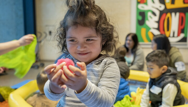 A White child with dark curly hair holds a toy in her hands as she plays in a Carter gallery.