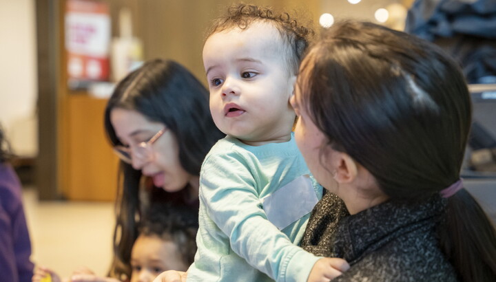 An adult holds a White baby with curly hair as they play in the Carter's Family Pop-up Space.