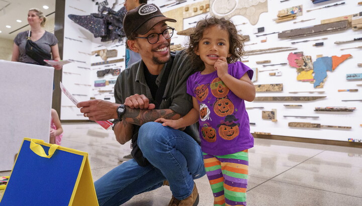 A medium-skinned man squats next to a medium-skinned child participating in an activity in a Carter gallery.