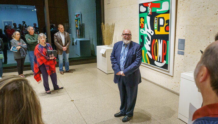 man standing in front of painting interacting with group of people