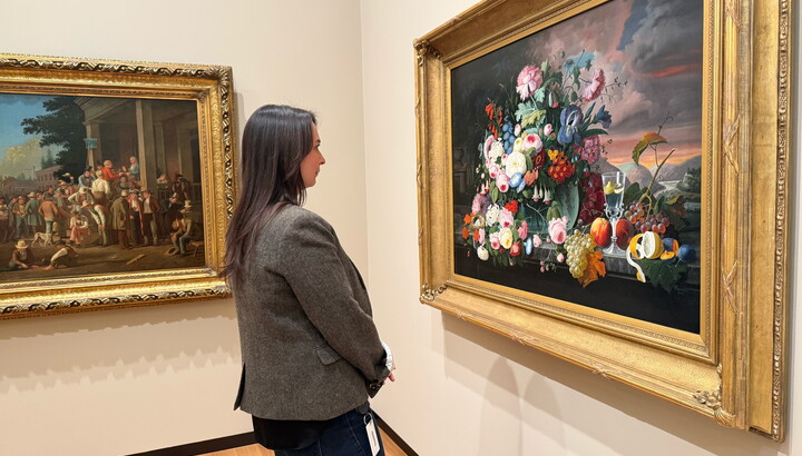 A White woman with long dark hair looks at a floral still life painting in a Carter gallery.